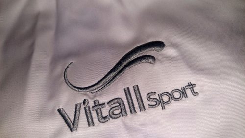 Zbliżenie srebrnego haftu logo Vitall Sport na koszuli
