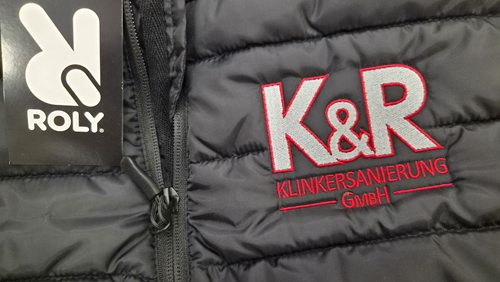 Zbliżenie haftowanego logo K&R Klinkersanierung na pikowanej kamizelce