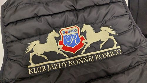 Zbliżenie na wielokolorowy haft logo Klubu Jazdy Konnej Romico na czarnej kamizelce