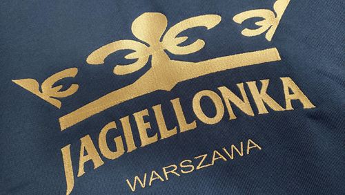 Zbliżenie dużego haftowanego logo złotą nicią na bluzie Jagiellonki Warszawa